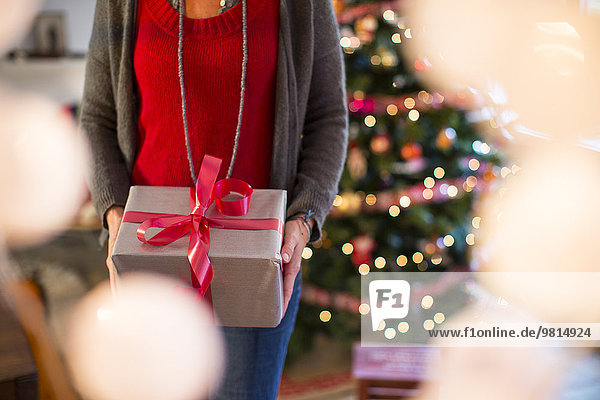 Abgeschnittene Aufnahme einer reifen Frau mit Weihnachtsgeschenk im Wohnzimmer