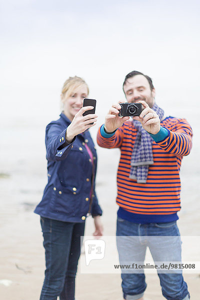 Couple outdoors  taking photographs using camera and smartphone