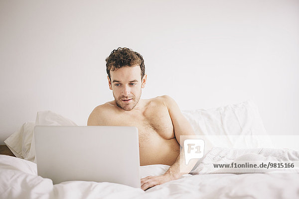 Junger Mann im Bett liegend mit Laptop