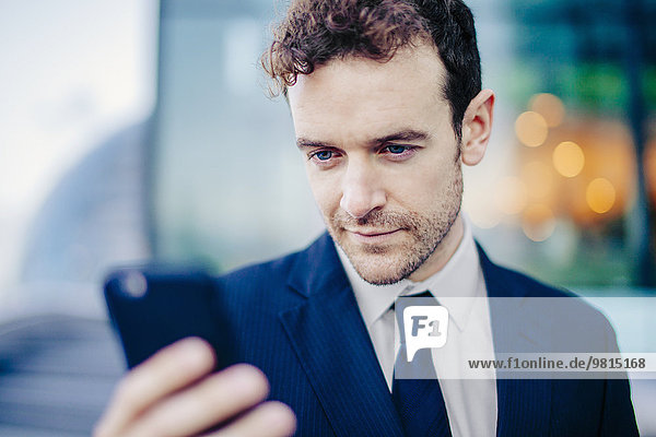 Geschäftsmann SMS auf dem Smartphone vor dem Büro