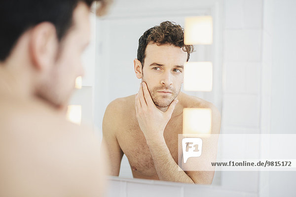Junger Mann überprüft sein Gesicht im Badezimmerspiegel