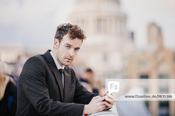 Businessman texting on smartphone whilst leaning on millennium bridge  London  UK
