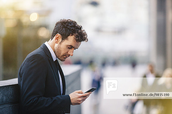 Businessman reading smartphone texts on city street