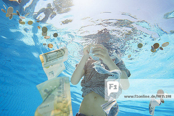 Unterwasseransicht des Jungen im Schwimmbad,  der sich die Euro-Währung schnappt.