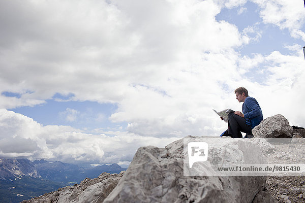 Male hiker sitting on top of mountain rock reading map  Peitlerkofel  South Tyrol  Italy