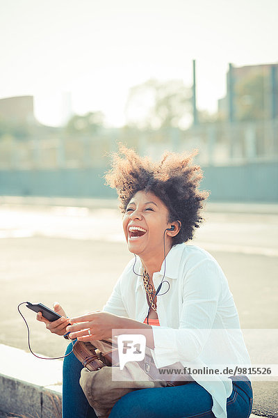 Junge Frau lacht und hört Smartphone-Musik auf dem Stadtparkplatz