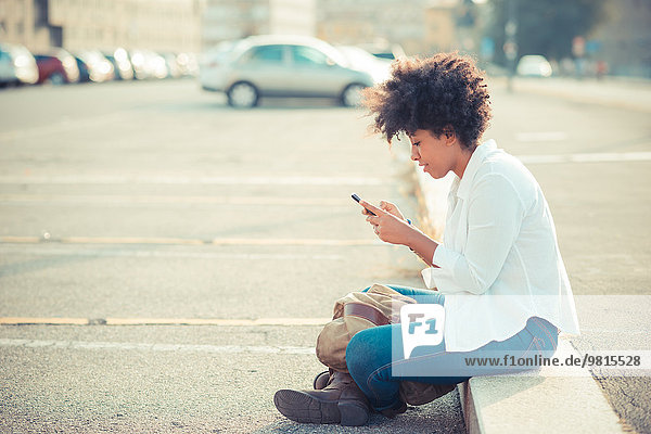 Junge Frau beim SMSen auf dem Smartphone auf dem Stadtparkplatz
