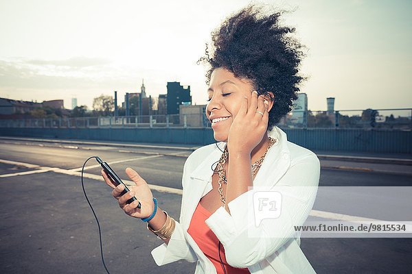 Junge Frau hört Smartphone-Musik auf dem Dach des Parkplatzes
