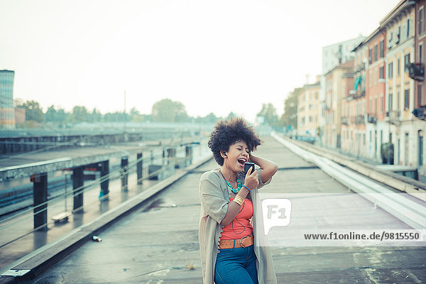 Junge Frau singt zu Musik vom Smartphone im städtischen Industriegebiet