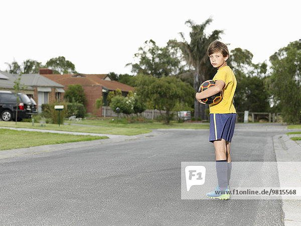 Porträt des mürrischen Jungen mit Fußball auf der Vorstadtstraße