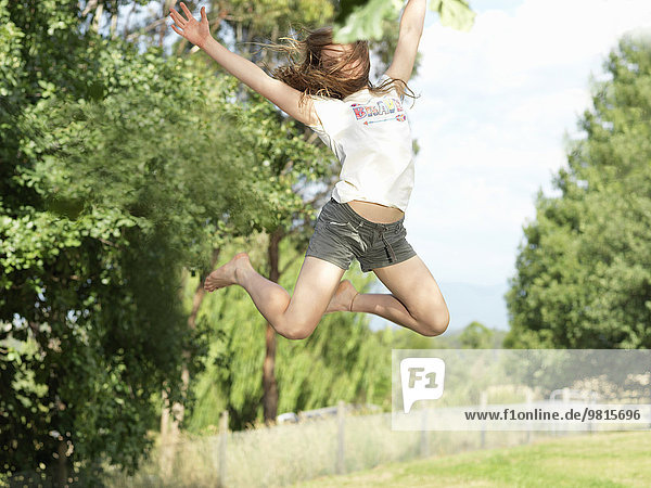 Teenager-Mädchen springt mit ausgestreckten Armen  in der Luft  im Freien