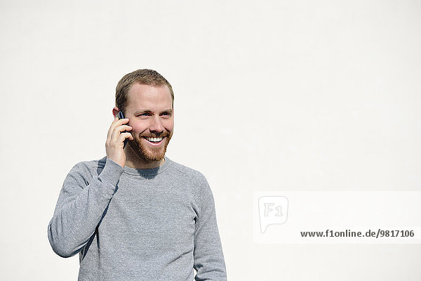 Porträt eines jungen Mannes beim Telefonieren mit Smartphone vor weißem Hintergrund