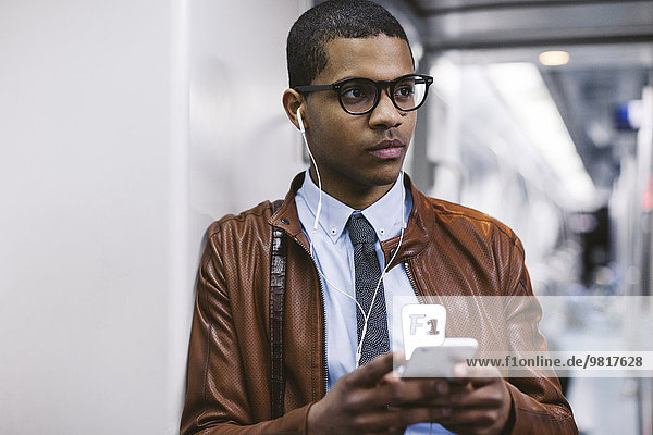Portrait of businessman with smartphone and earphones hearing music on the subway train