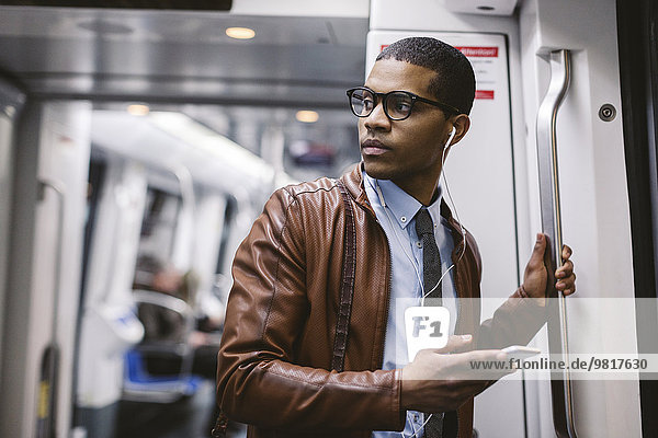 Geschäftsmann mit Smartphone und Kopfhörer  der Musik in der U-Bahn hört.