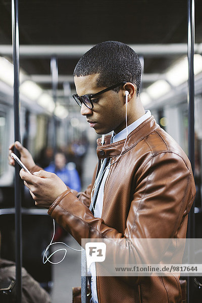 Portrait of businessman with smartphone and earphones hearing music on the subway train