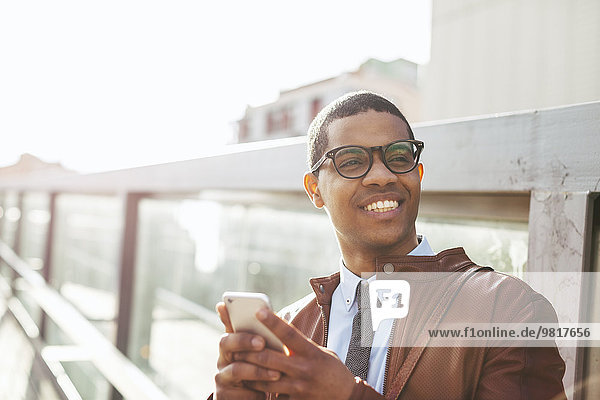 Portrait of smiling businessman with smartphone wearing leather jacket and glasses