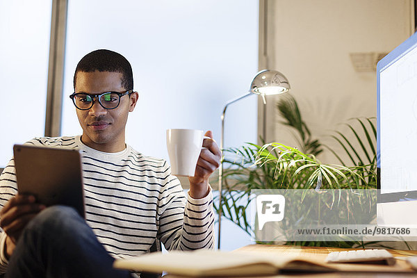 Junger kreativer Mann mit Mini-Tablette bei einer Kaffeepause in seinem Home-Office