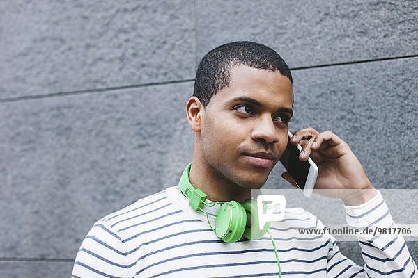 Portrait eines jungen Mannes mit grünen Kopfhörern beim Telefonieren mit Smartphone