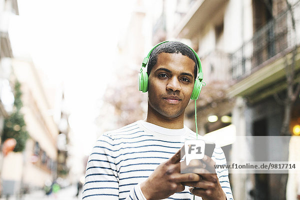 Spain  Barcelona  portrait of smiling young man hearing music with green headphones on street