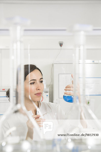 Junge Wissenschaftlerin im Labor beurteilt blaue Flüssigkeit in der Flasche
