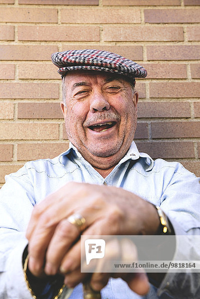 Lachender alter Mann mit Baskenmütze auf dem Rohrstock