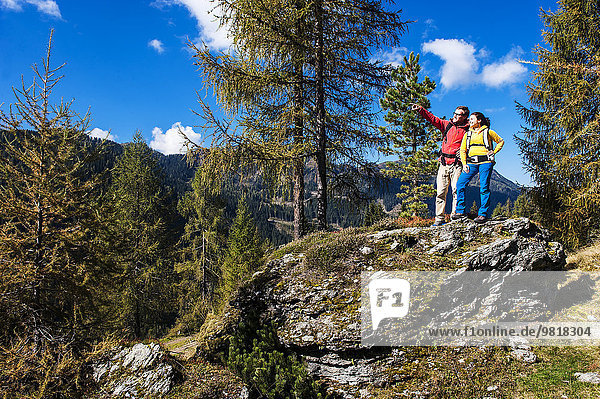 Österreich  Altenmarkt-Zauchensee  junges Paar auf einem Felsen stehend mit Blick auf die Umgebung