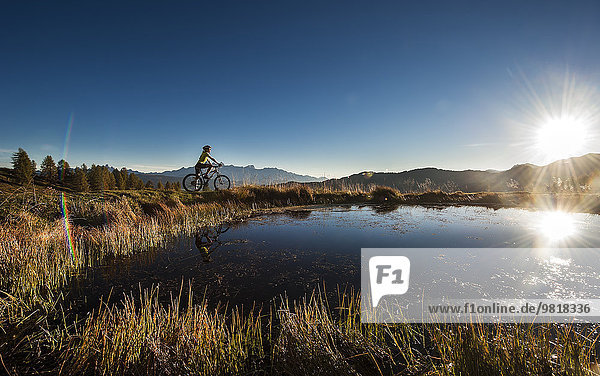 Österreich  Altenmarkt-Zauchensee  junge Frau auf dem Mountainbike bei Sonnenaufgang