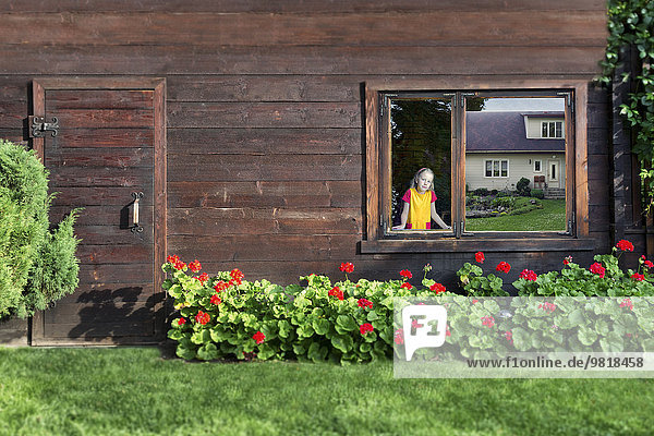 Estland  Mädchen schaut durch das Fenster einer Blockhütte