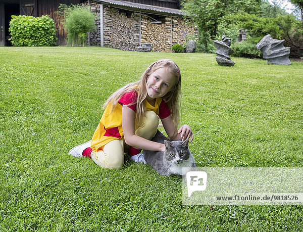 Estland  lächelndes Mädchen auf dem Rasen sitzend  streichelnde Katze