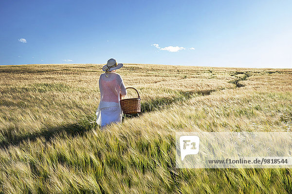 Estland  Frau  die in einem Getreidefeld mit Korb in der Hand läuft