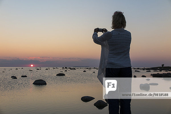 Estland,  Kaesmu,  Frau beim Fotografieren des Sonnenuntergangs mit Smartphone