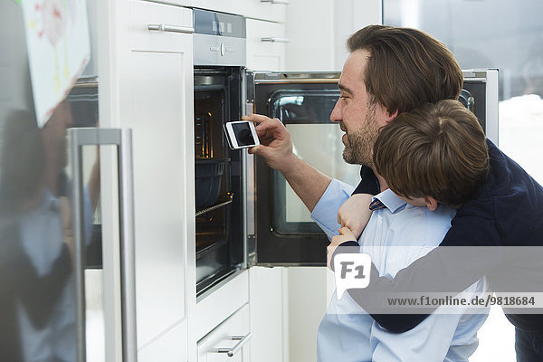 Vater und Sohn fotografieren Kuchen im Ofen mit Smartphone