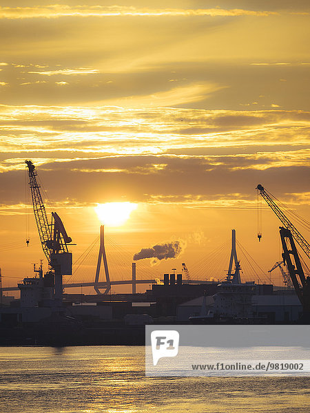 Deutschland,  Hamburg,  Silhouetten von Hafenkranen bei Sonnenuntergang,  Koehlbrandbrücke im Hintergrund