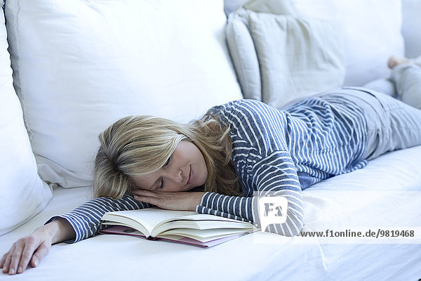 Frau auf der Couch liegend mit einem Buch schlafend