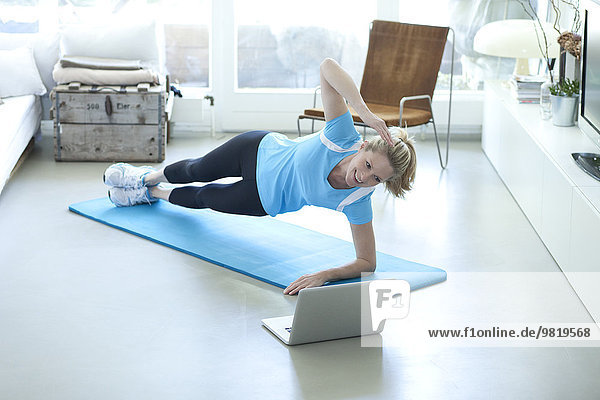 Woman looking at laptop exercising on gym mat in living room