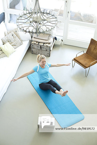 Woman with laptop exercising on gym mat in living room
