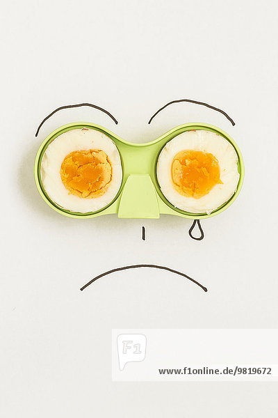 Two halves of an egg in green holder with sad face drawn around it