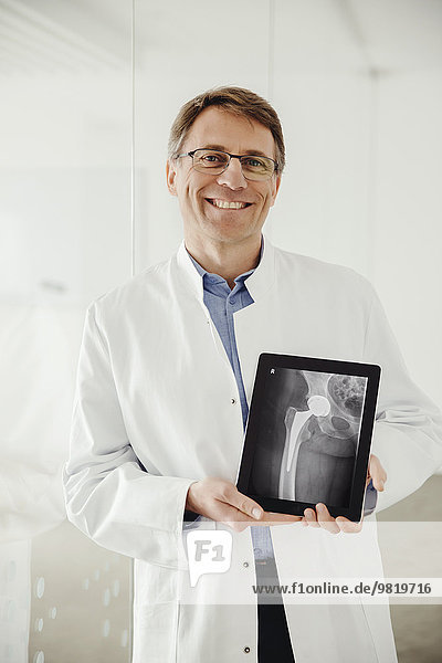 Mature man in lab coat presenting an x-ray scan on his digital tablet