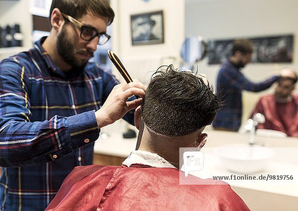 Hairdresser shaving young man's hair in a barbershop