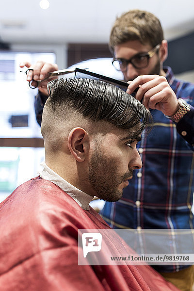 Hairdresser cutting young man's hair in a barbershop