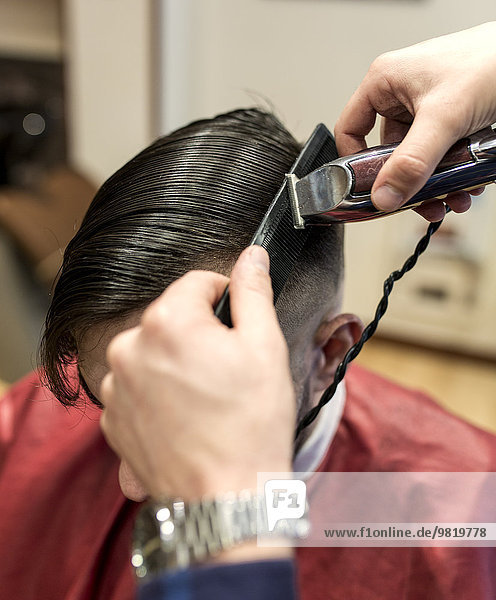 Friseur beim Rasieren der Haare eines jungen Mannes in einem Friseursalon