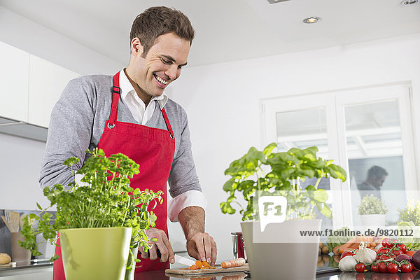 Smiling man cutting carrots in kitchen