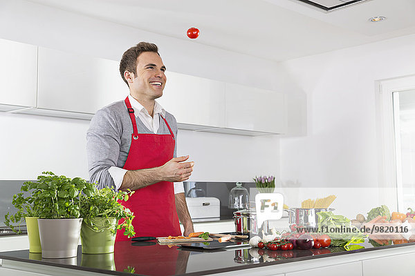 Lächelnder Mann jongliert mit Tomaten in der Küche