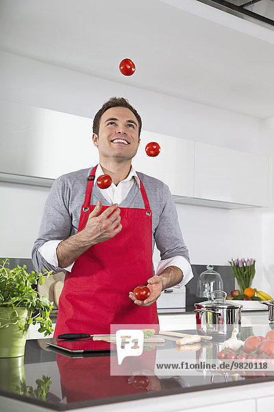 Smiling man juggling with tomatoes in kitchen