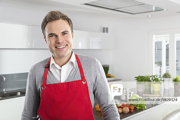 Portrait of smiling man with red apron in kitchen
