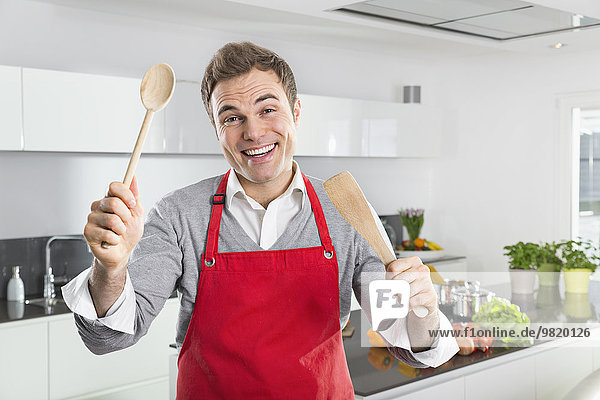 Portrait of smiling man with red apron and kitchen utensils