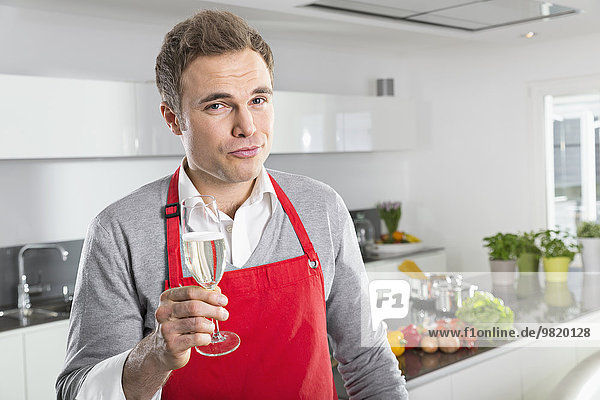Portrait of man offering glass of sparkling wine in kitchen