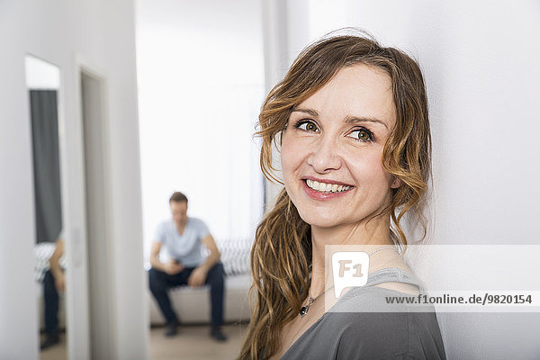 Porträt einer lächelnden Frau  die im Flur steht  während der Mann im Hintergrund wartet.