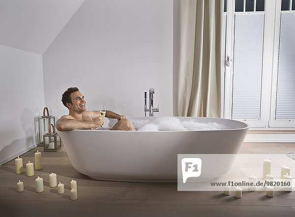 Mann entspannt in der Badewanne bei einem Glas Champagner