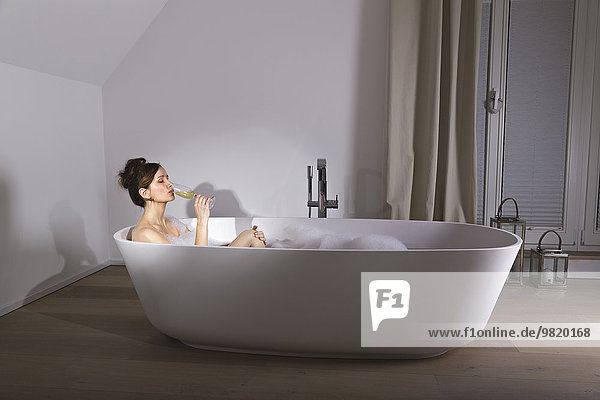 Frau entspannt sich in moderner Badewanne und trinkt Champagner